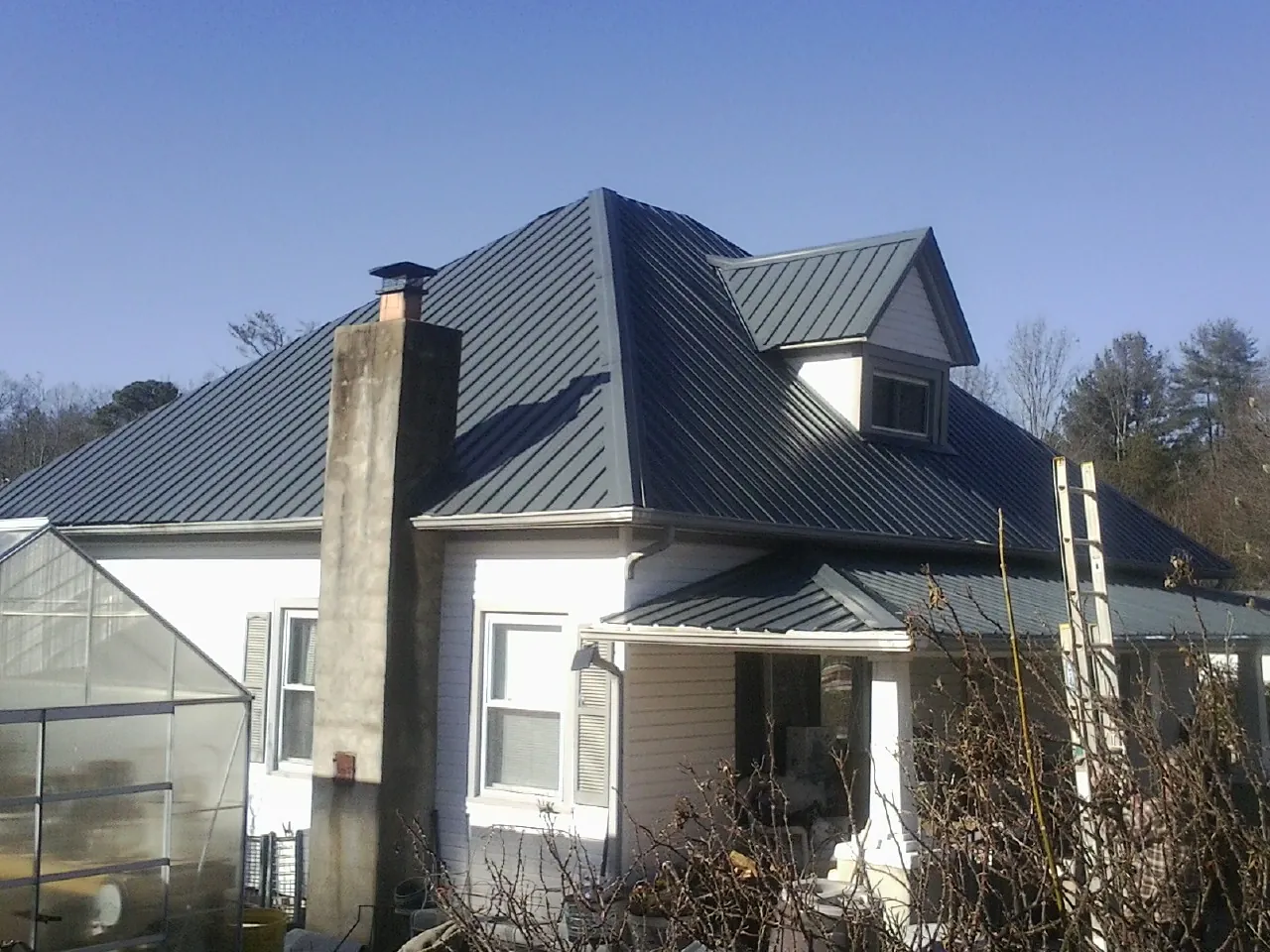Dark blue standing seam metal roof on a white farmhouse with dormer — Slate & Tile Roof Repair by Roofing Brothers in Edgerton