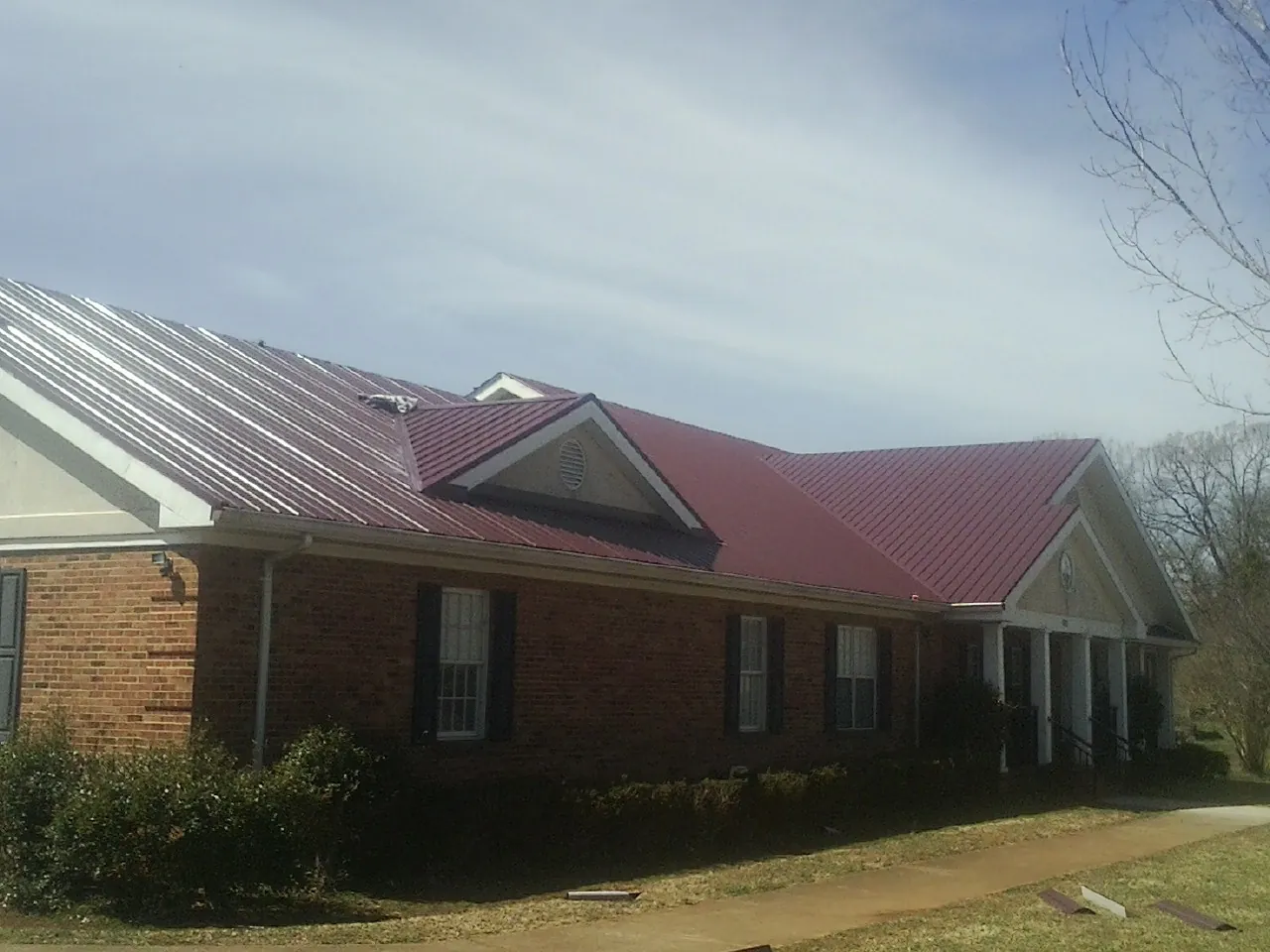 Red metal roof with gabled entries on a long brick building, from a Hail Damage Roof Repair job in Edgerton